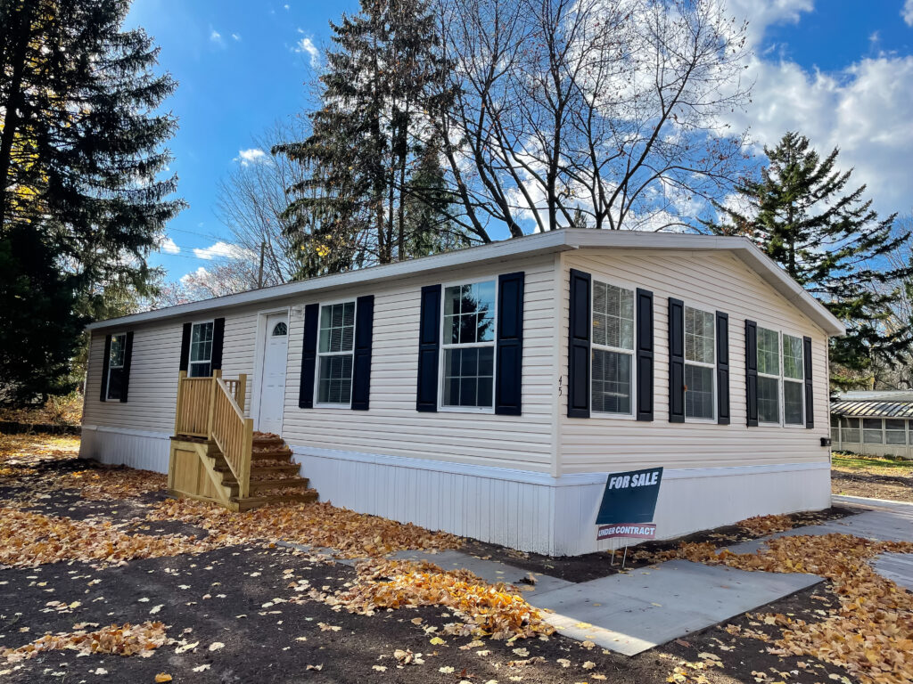 Brand new prefab mobile home with for sale yard sign post, colorful fall foliage near Rochester, New York